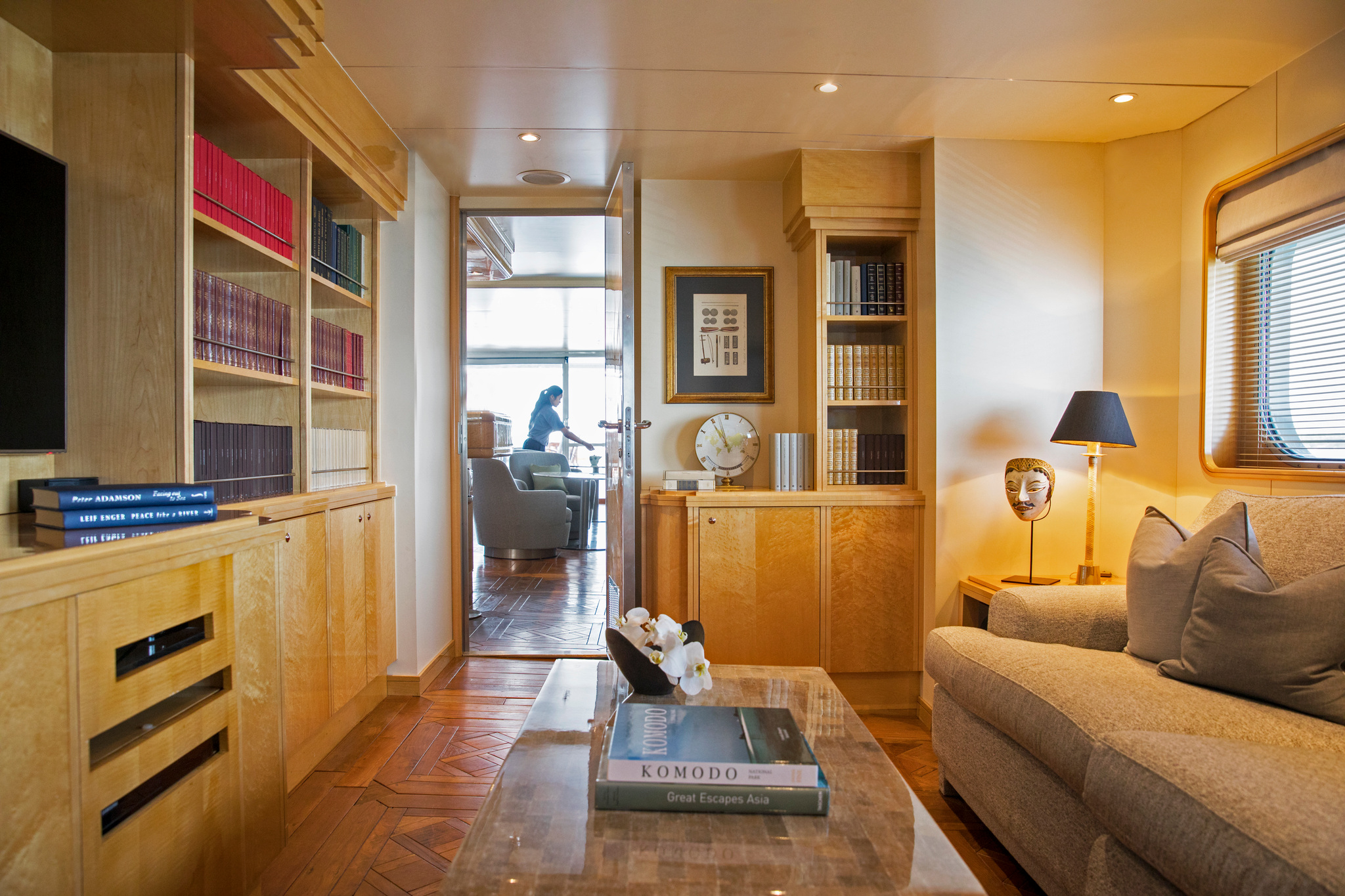 The library and TV room, with bookcases, a sofa and a coffee table stacked with books