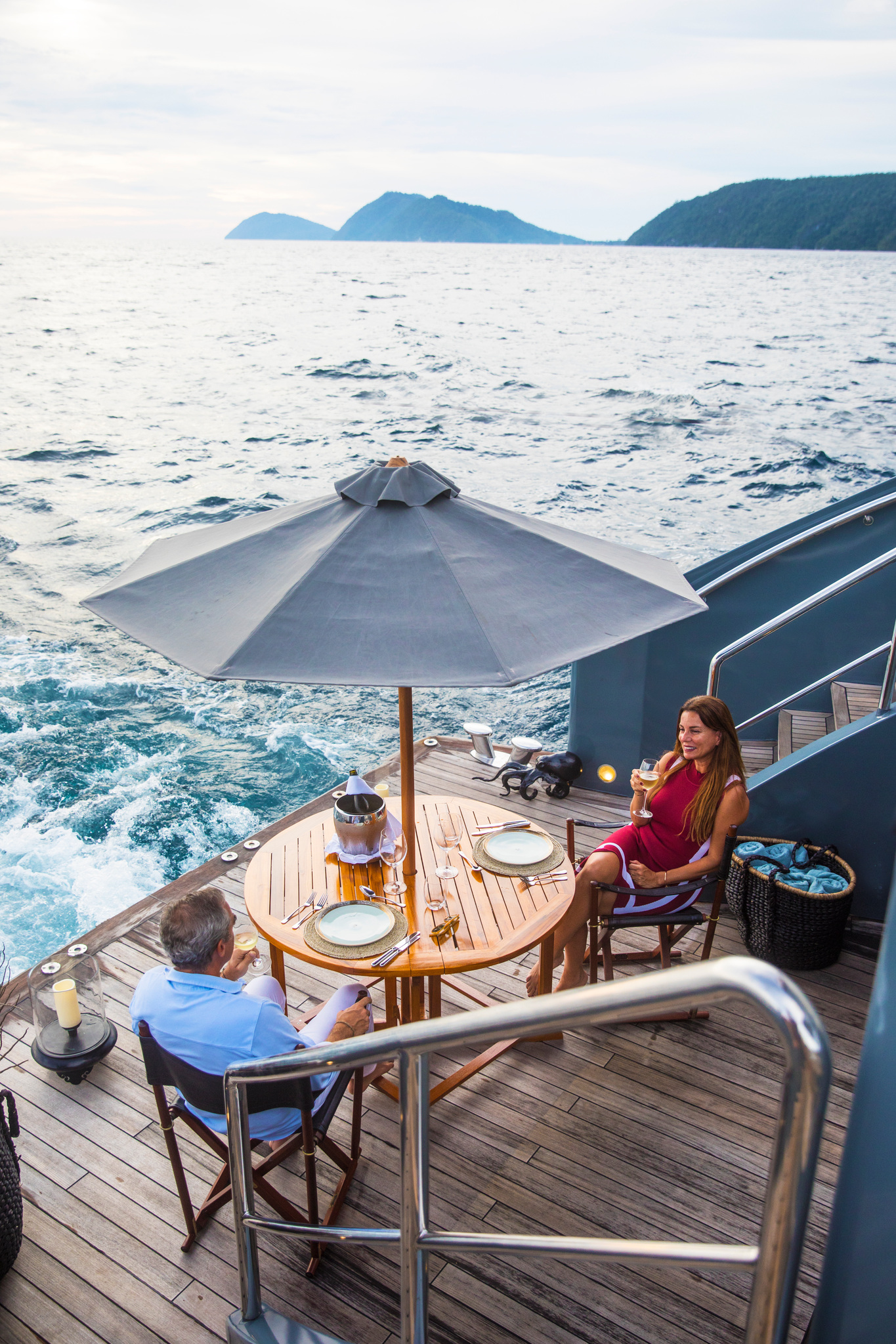 Two guests at lunch under a parasol, the wake and islands behind