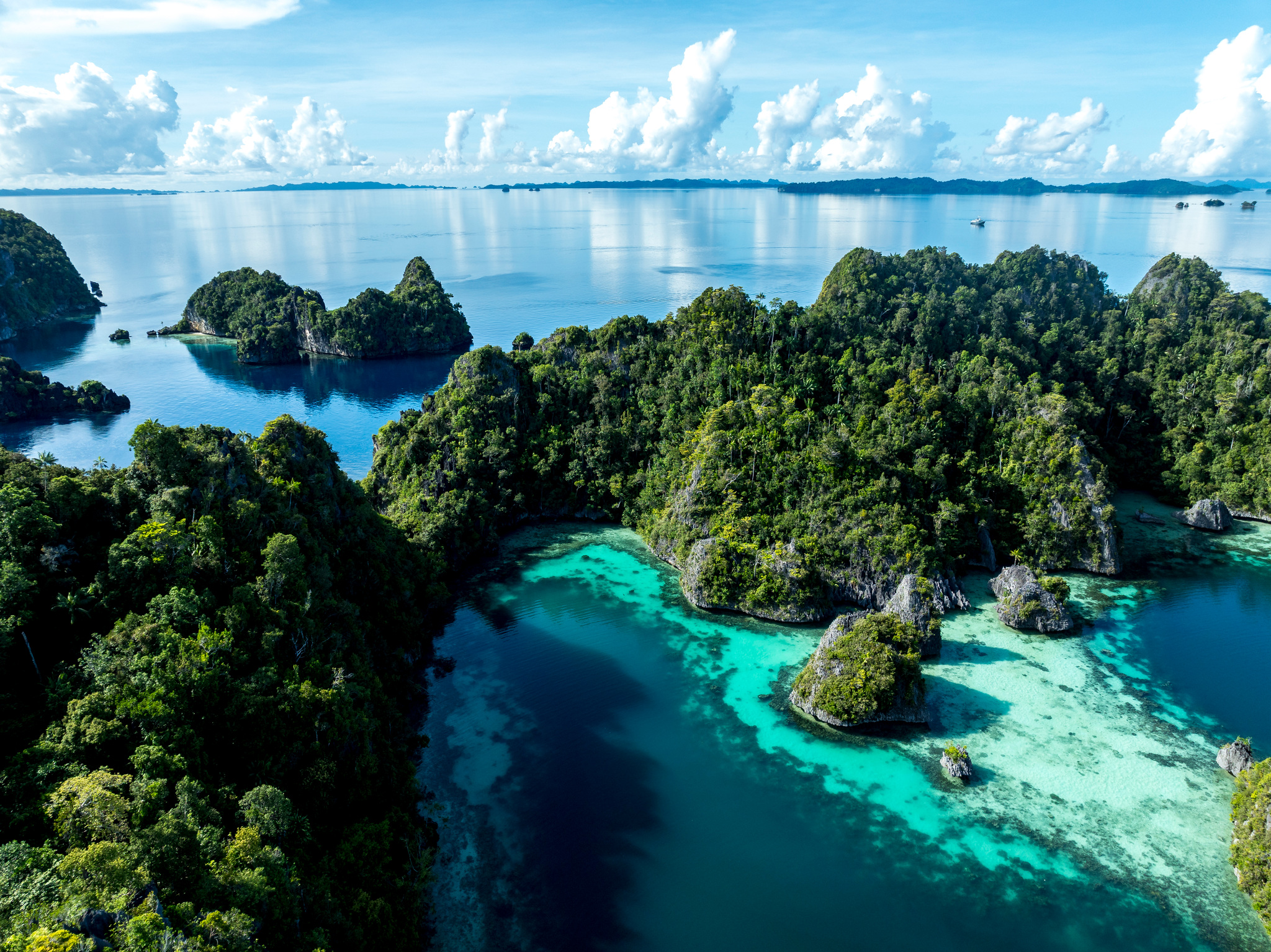 A sheltered lagoon of pale sand and coral among forested limestone islands in Misool