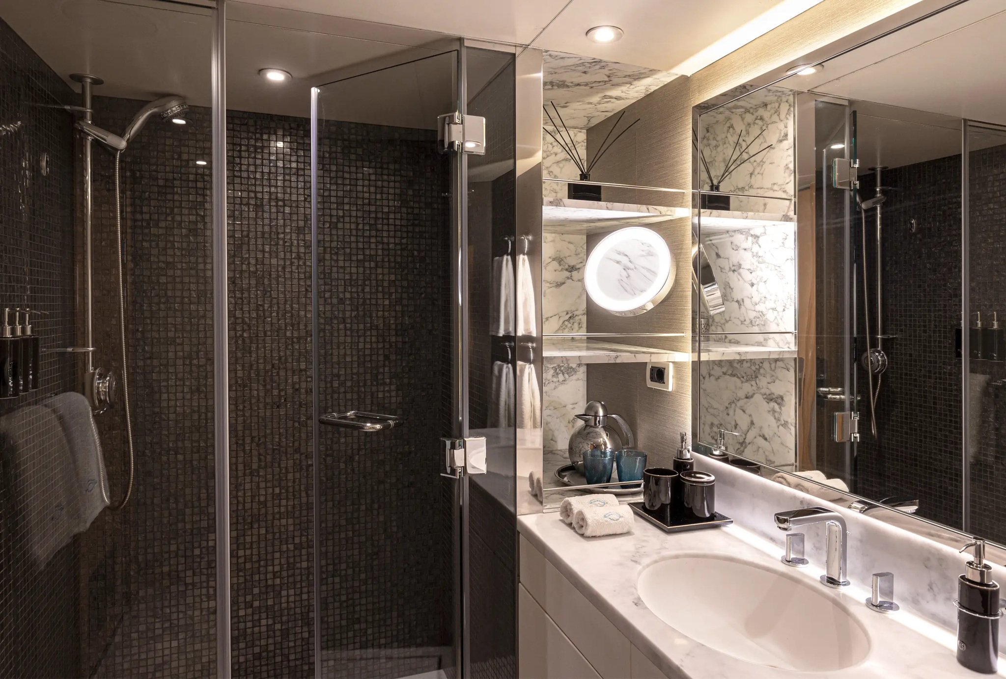 The bathroom of cabin 203, with a glass-walled shower, dark mosaic tiles and a marble basin