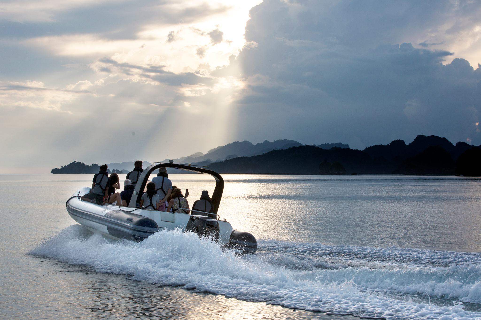 A tender of guests at speed under sunbeams, dark islands on the horizon