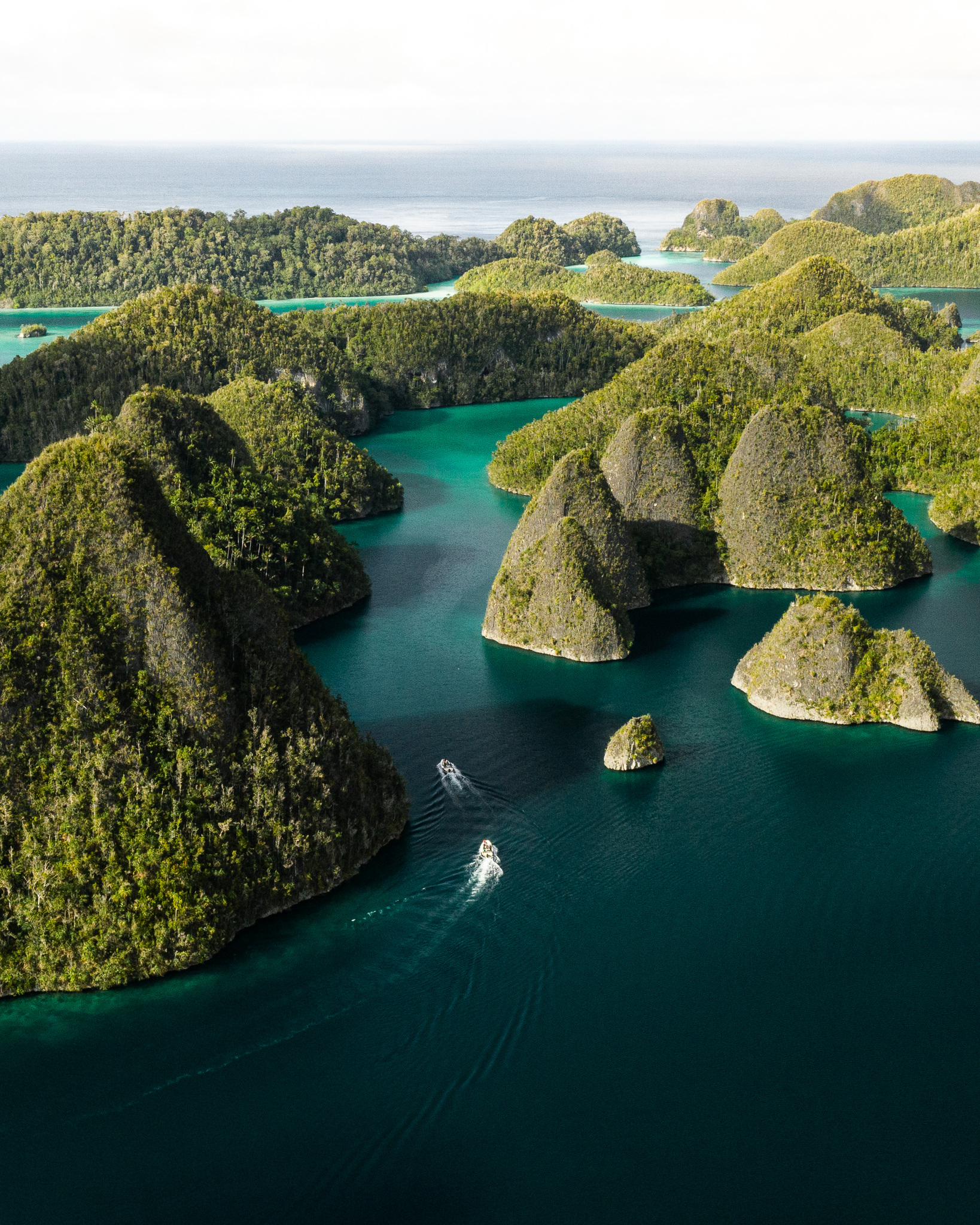 Rounded, forested karst islets at Wayag, with two tenders between them