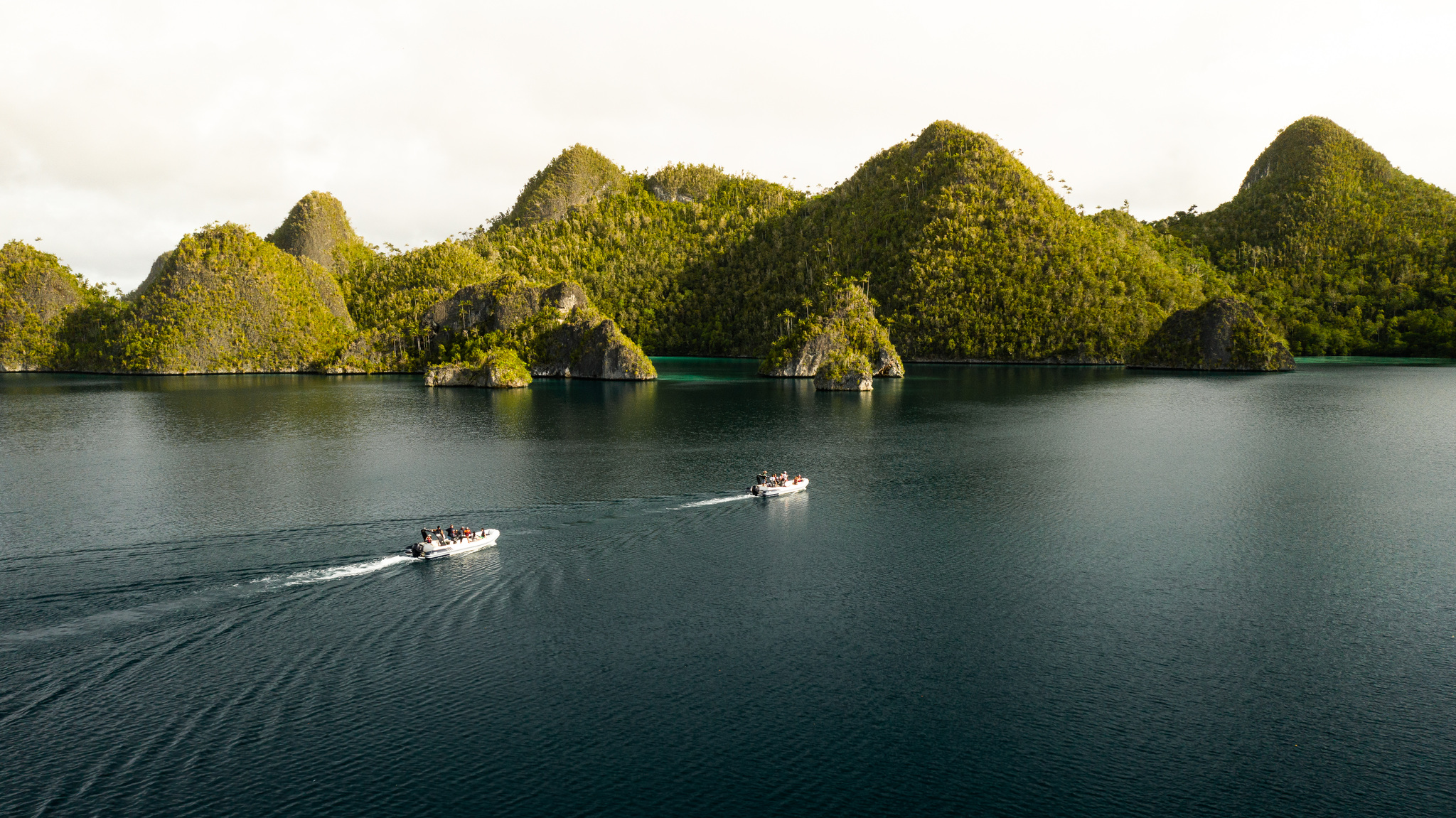 Two tenders crossing calm water below the forested peaks of Wayag