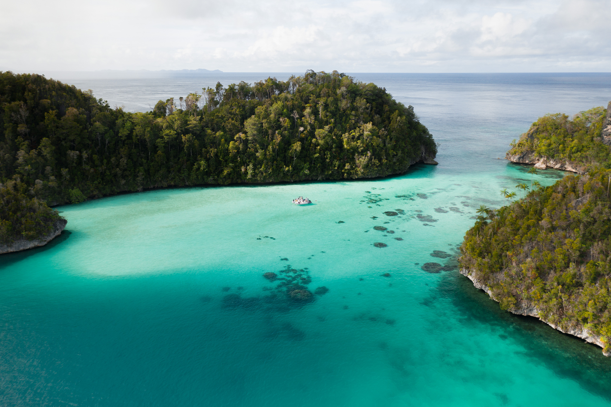 A sandy turquoise lagoon enclosed by forested islands at Wayag, with a tender at anchor
